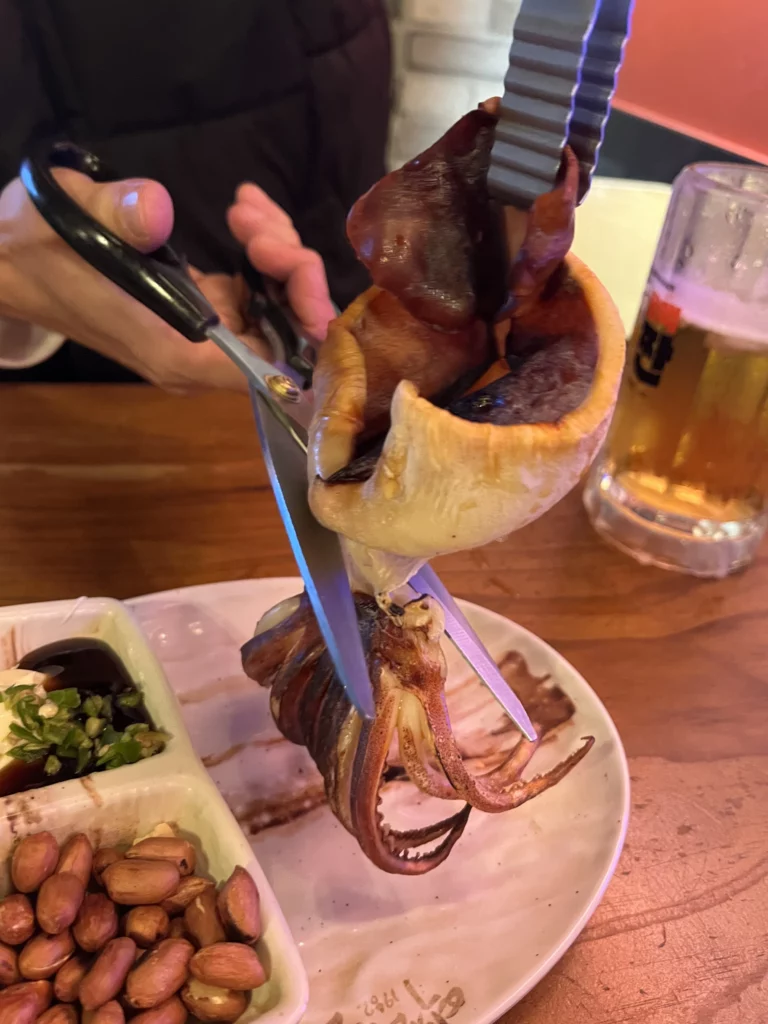Customer tearing dried squid ojingeo-ip anju with scissors paired with Korean iced beer at Yeokjeon Halmae Maekju.