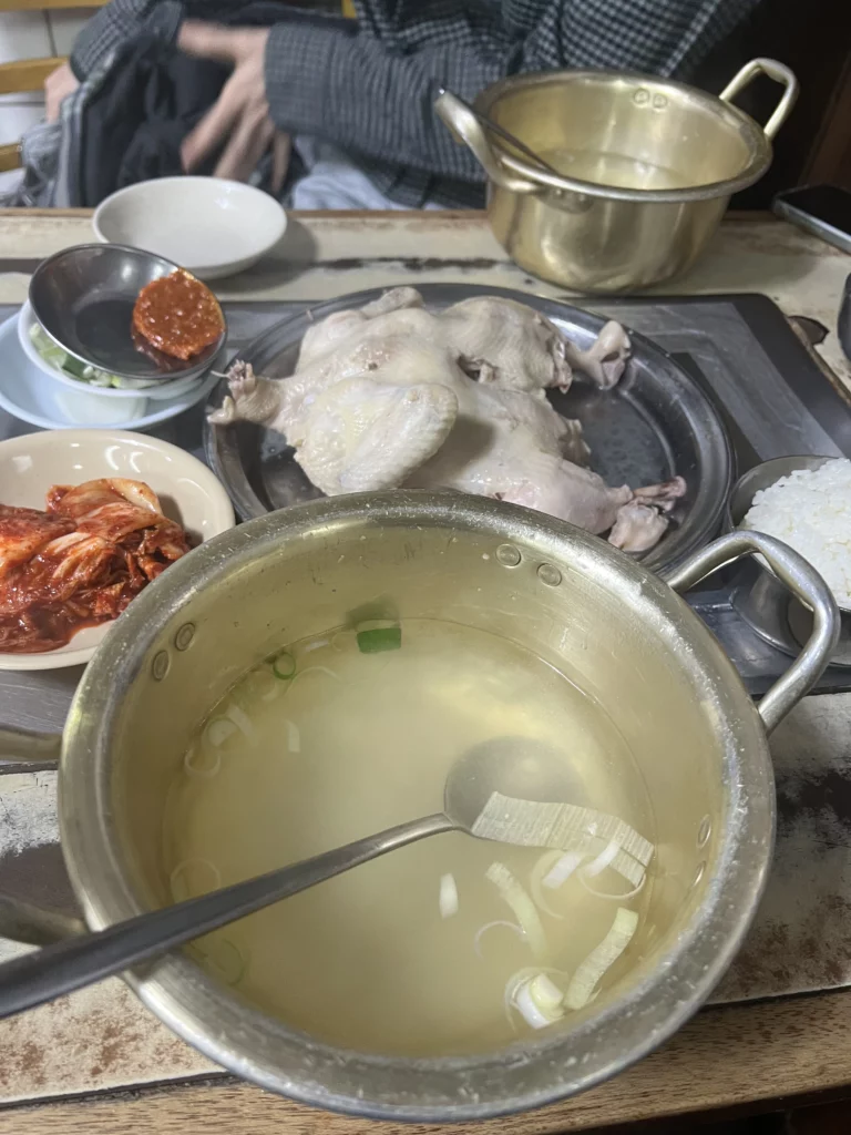 Complete baeksuk baekban set meal at Sarangbang Kalguksu featuring whole chicken, garlic-infused milky broth, rice, kimchi, and traditional Korean banchan side dishes for 9000 won.