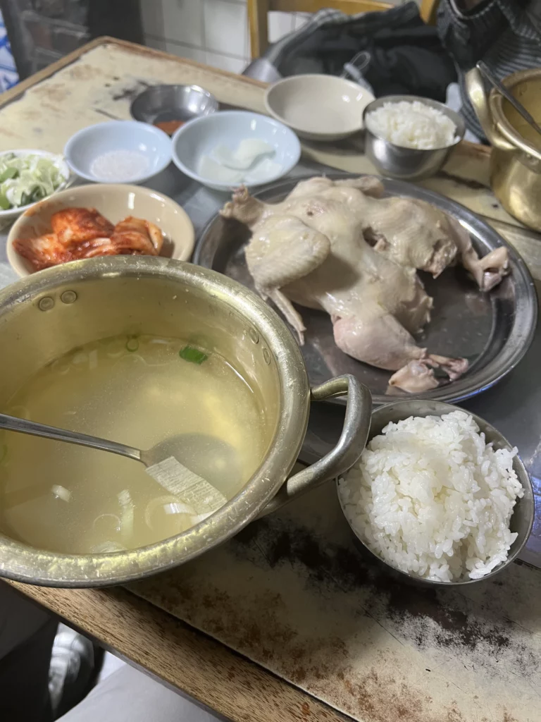 Complete baeksuk baekban set meal at Sarangbang Kalguksu with whole dak baeksuk chicken, garlic-infused broth, steamed rice, kimchi, and traditional Korean banchan side dishes in Seoul Chungmuro.