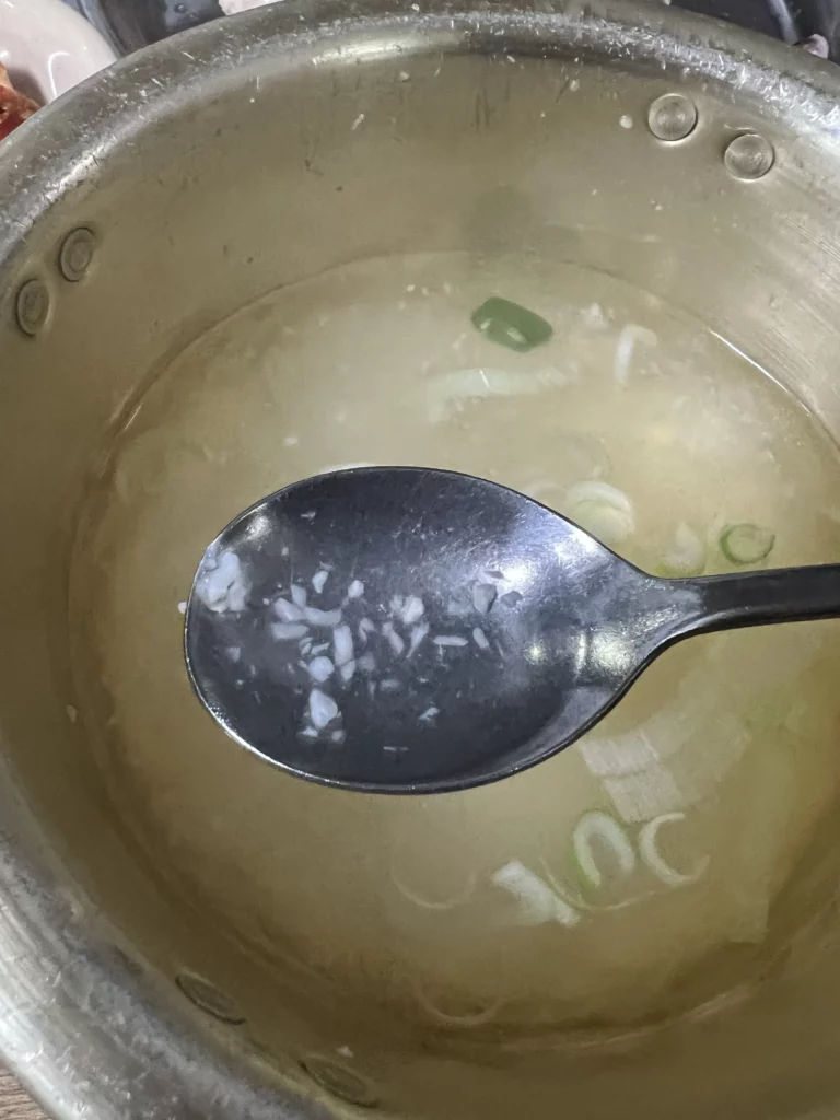 Rich garlic-infused dak baeksuk broth with green onions in metal pot at Sarangbang Kalguksu Blue Ribbon recognized Korean chicken soup restaurant in Seoul.