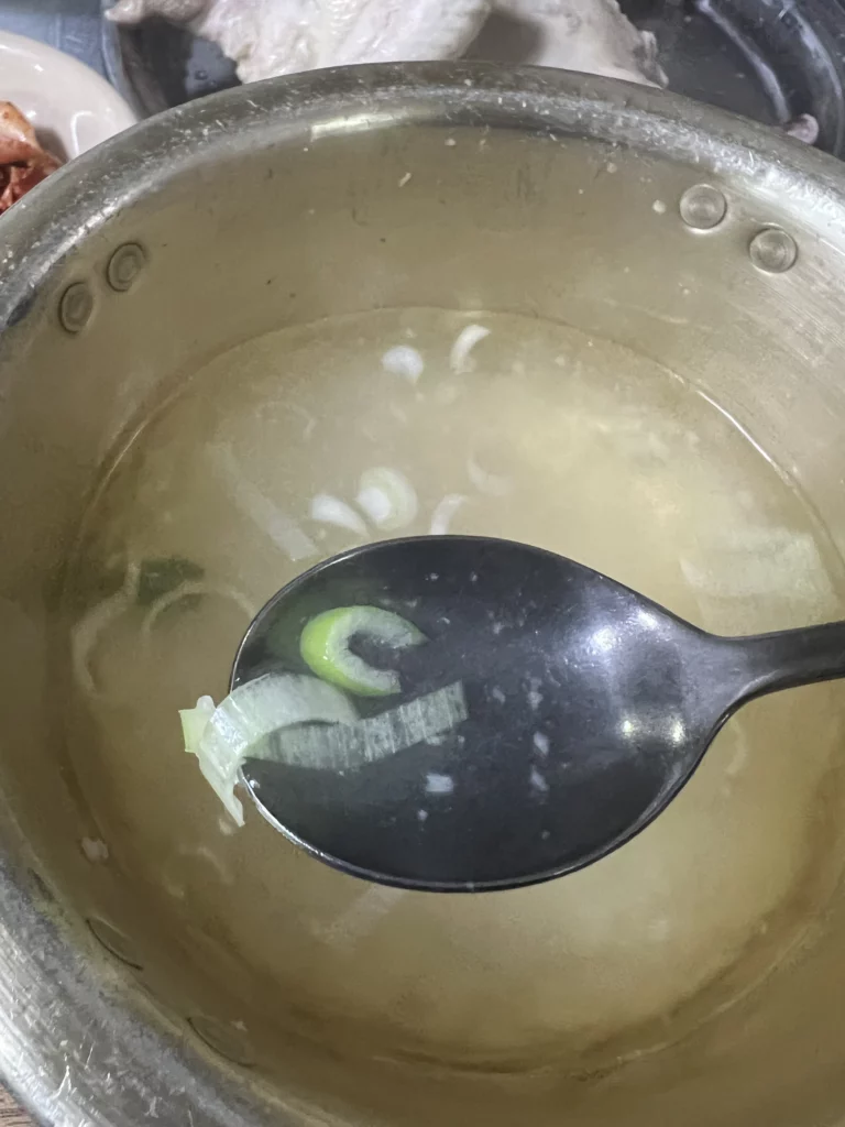 Garlic-infused dak baeksuk broth with green onions served at Sarangbang Kalguksu Blue Ribbon awarded Korean boiled chicken soup restaurant in Seoul Chungmuro.