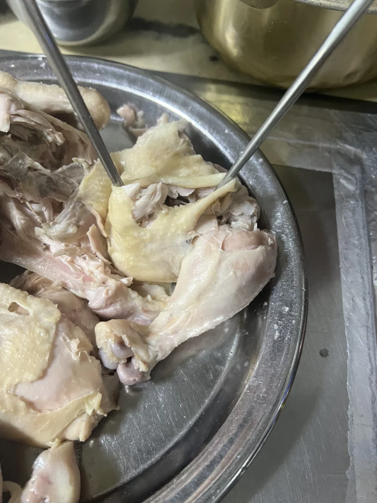 Tender shredded dak baeksuk chicken pieces torn with chopsticks on metal plate at Sarangbang Kalguksu traditional Korean boiled chicken soup restaurant in Seoul Chungmuro.