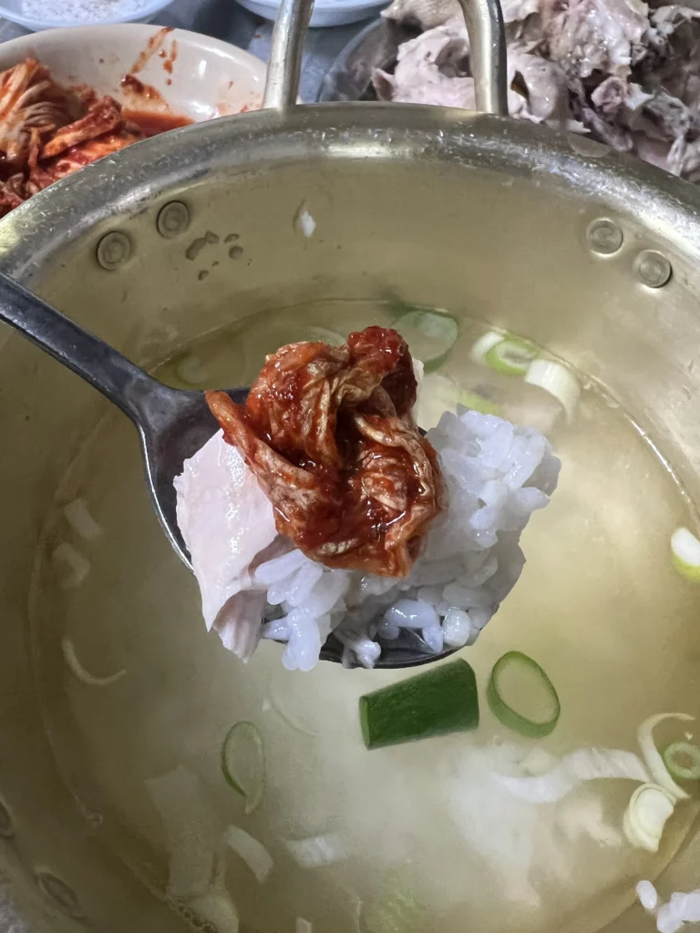 Rice being added to remaining dak baeksuk broth with kimchi and green onions to create traditional Korean chicken soup porridge at Sarangbang Kalguksu in Seoul.