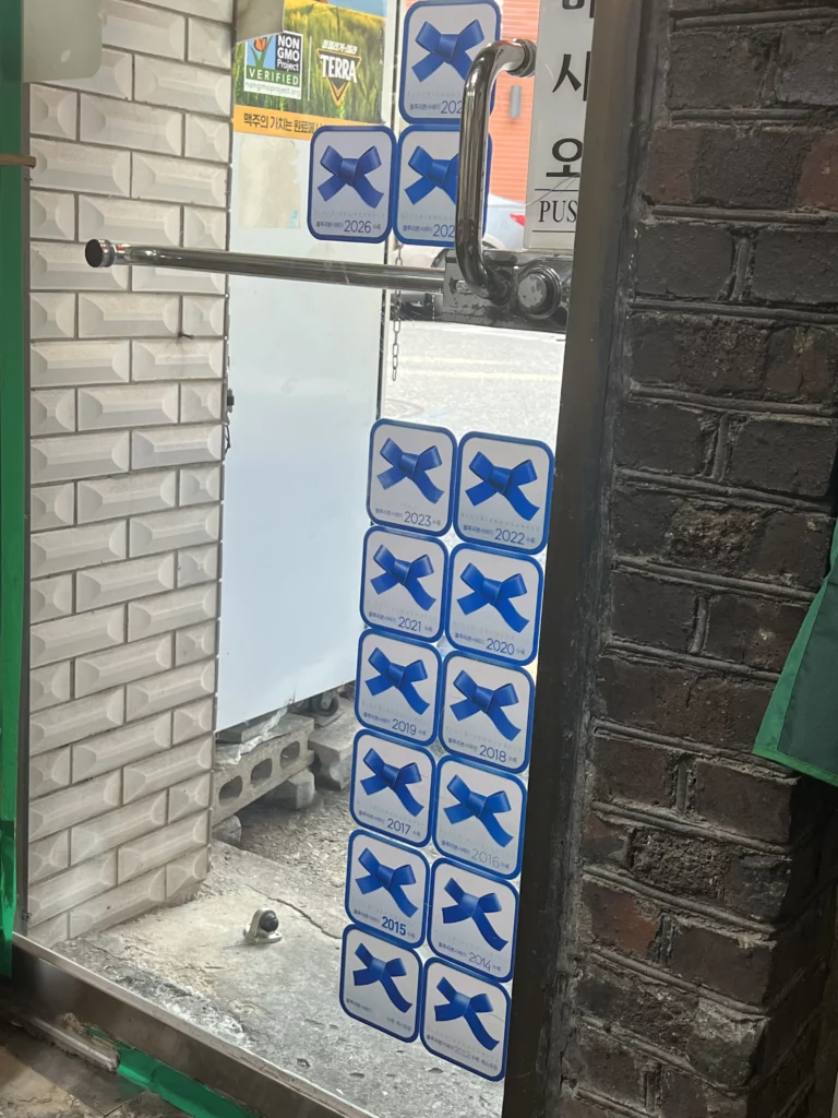 Blue Ribbon award stickers displayed at entrance of Sarangbang Kalguksu restaurant in Seoul Chungmuro showing continuous recognition since 2012 for authentic Korean dak baeksuk.