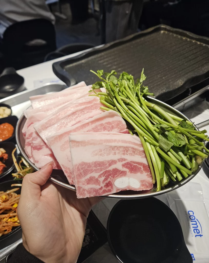 Frozen Samgyeopsal Korean BBQ plate featuring neatly stacked slices of frozen pork belly alongside fresh green vegetables, prepared and ready for grilling at the table.