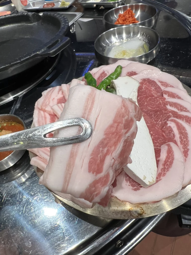 Thick-cut samgyeopsal pork belly and tofu being prepared for grilling at Moosik authentic Korean BBQ restaurant in Sinsa-dong Gangnam.
