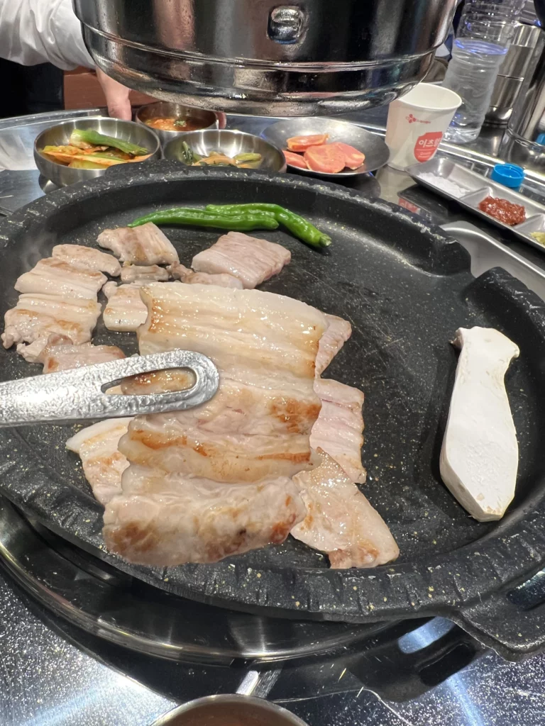 Grilled samgyeopsal pork belly pieces with green peppers and tofu cooking on hot plate at Moosik authentic Korean BBQ restaurant in Sinsa-dong Gangnam Seoul.