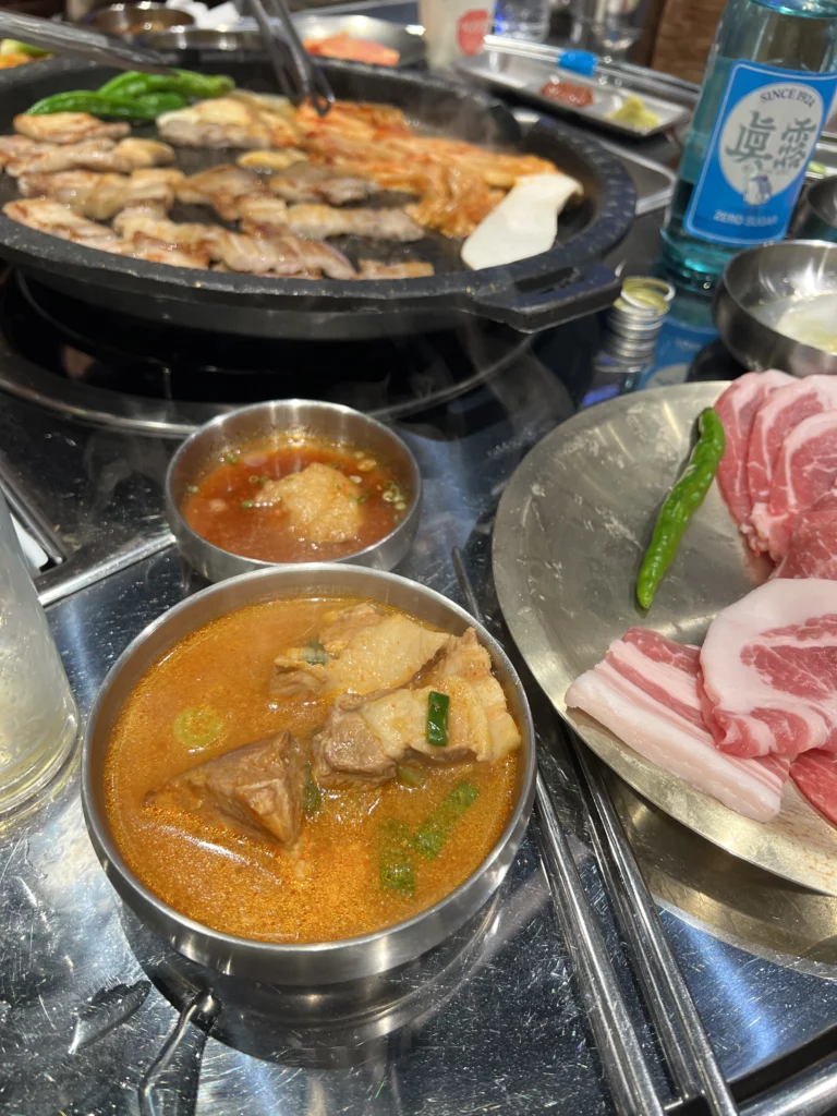 Korean stew jjigae with grilled samgyeopsal pork belly on grill and fresh meat platter at Moosik authentic Korean BBQ restaurant in Sinsa-dong Gangnam Seoul.