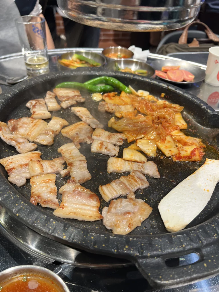 Grilled samgyeopsal pork belly with kimchi green peppers and tofu sizzling on grill at Moosik authentic Korean BBQ in Sinsa-dong Gangnam Seoul.