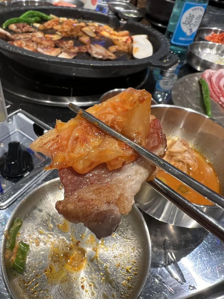 Chopsticks holding kimchi with grilled samgyeopsal pork belly at Moosik authentic Korean BBQ restaurant in Sinsa-dong Gangnam Seoul.