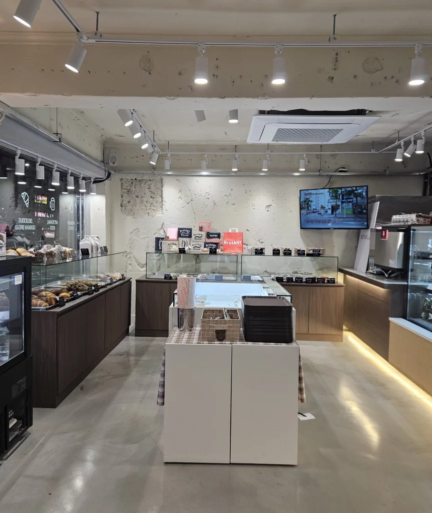 Minimalist bakery cafe interior with glass display counters, neatly arranged bread and pastries, warm lighting, and a clean modern design.