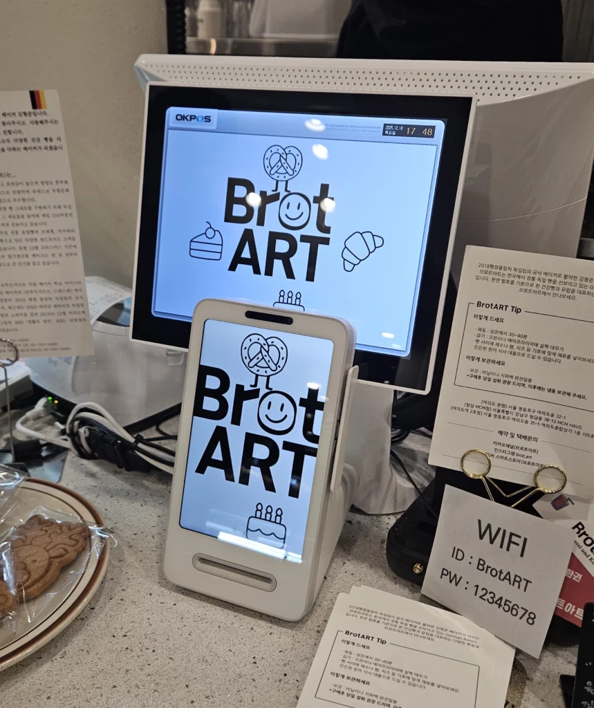 Close-up of the checkout counter inside a bakery cafe, showing branded POS screen, digital payment device, baked goods, and cozy café details.