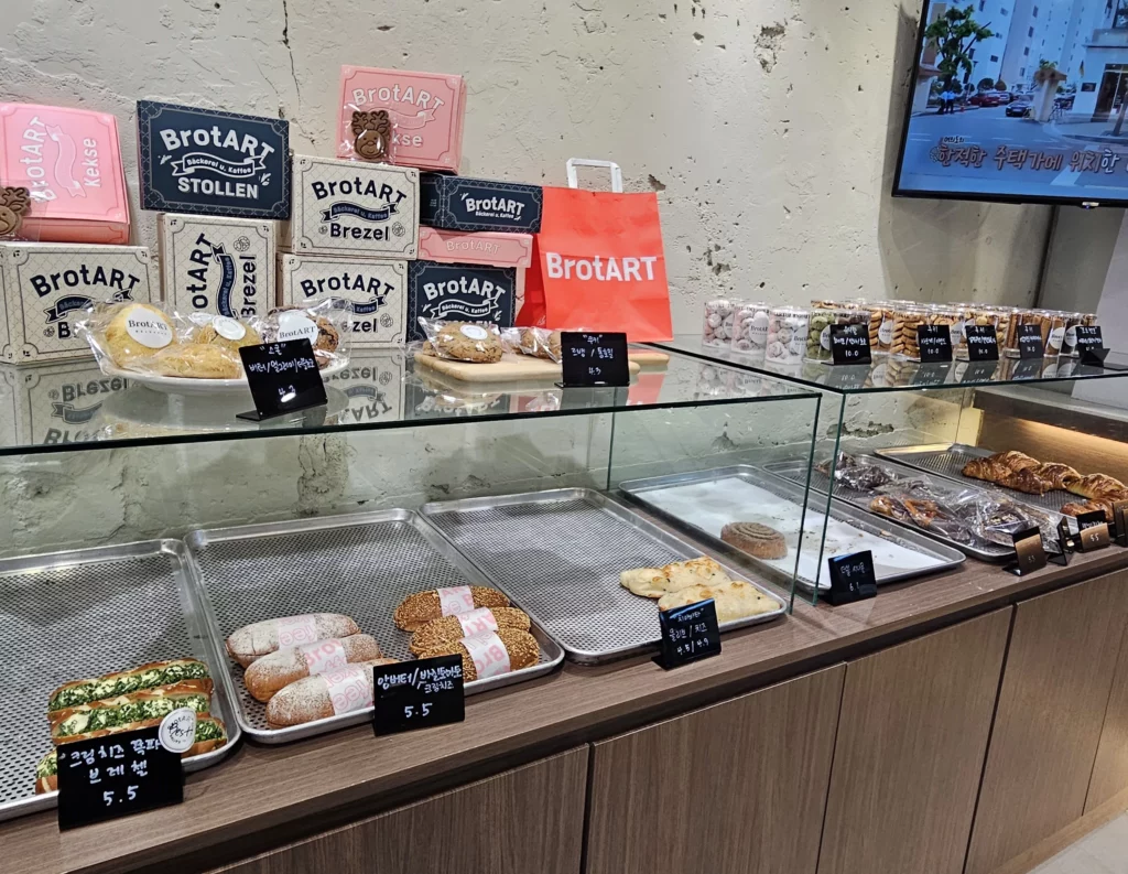 Interior of a bakery cafe with artisanal bread, cookies, and packaged baked goods displayed on wooden counters and glass shelves.