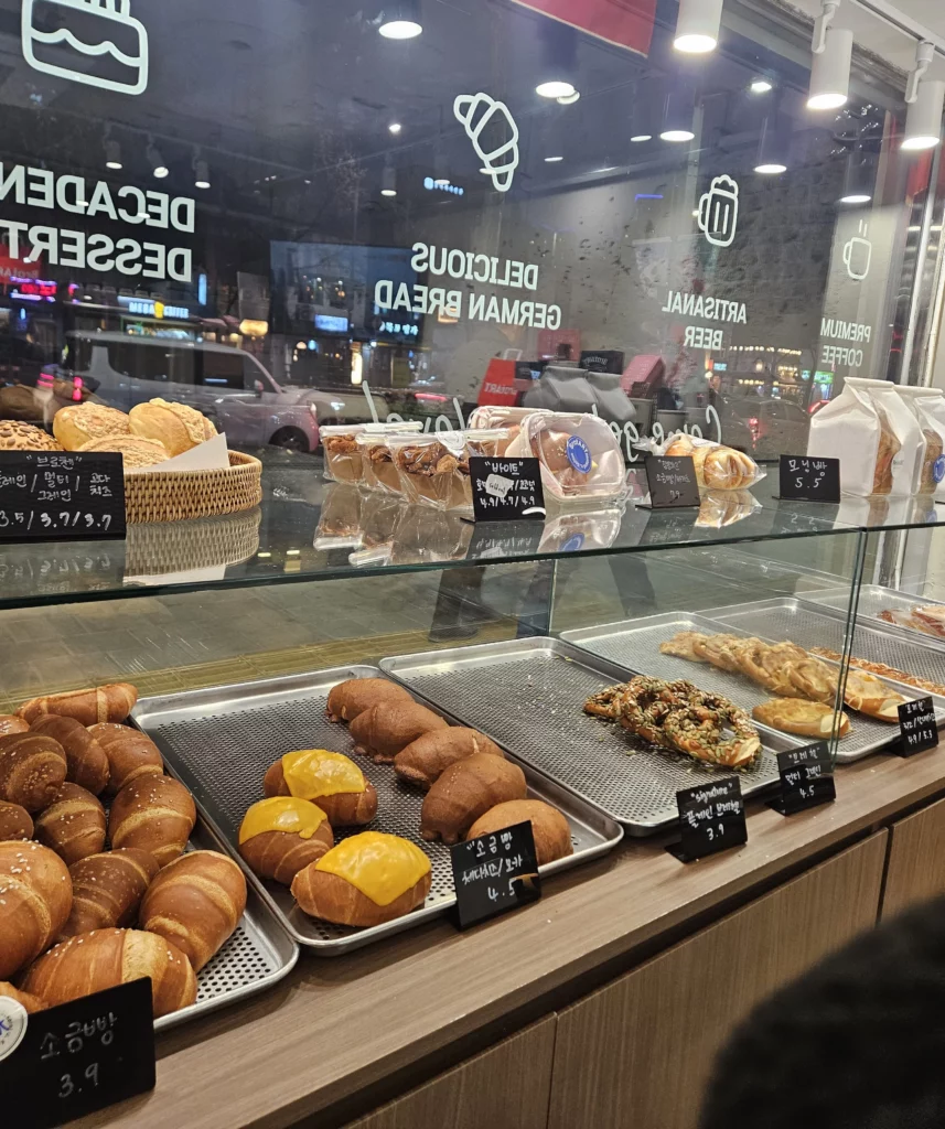 Evening view inside a bakery cafe showcasing freshly baked bread and pastries displayed near a window with city lights outside.