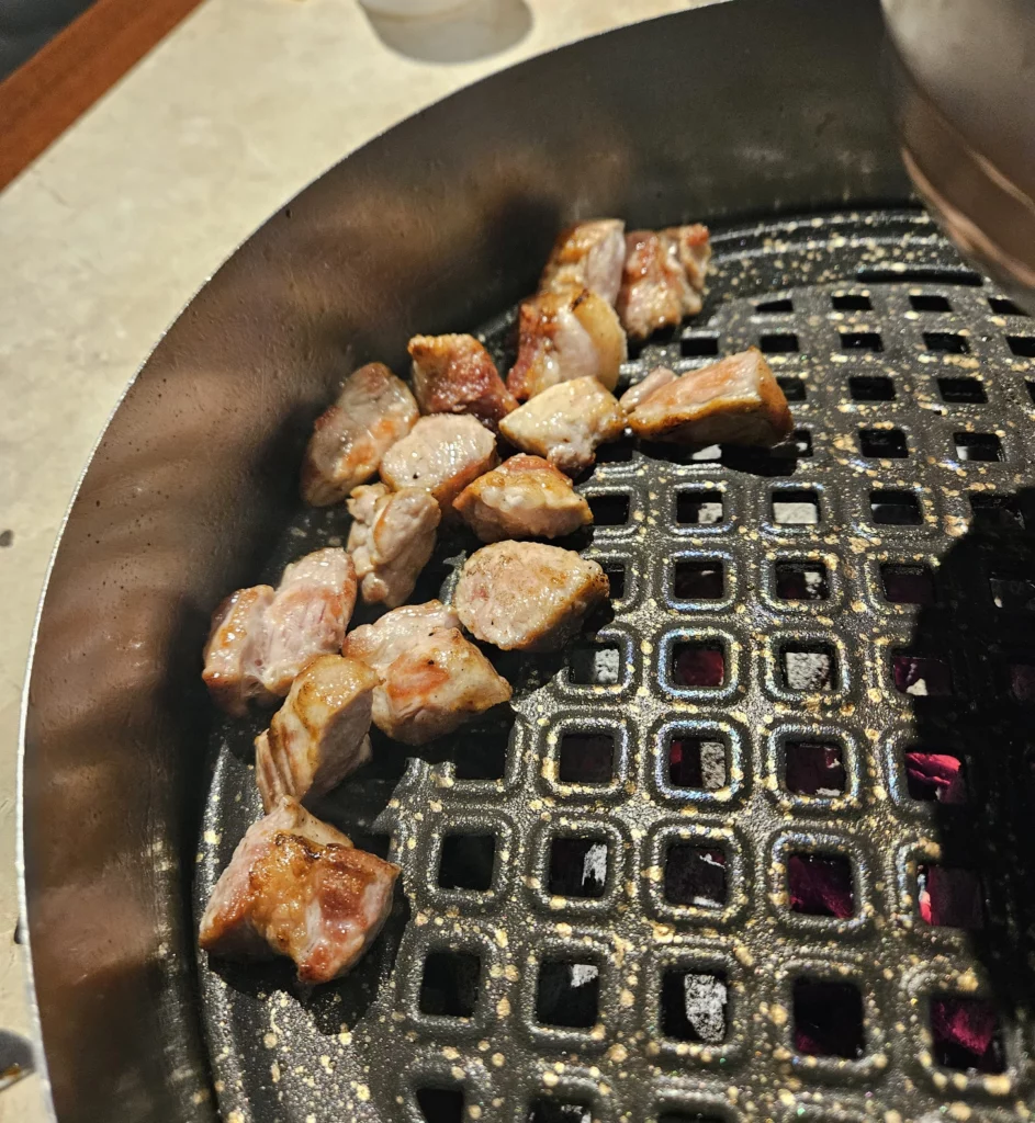 Bite-sized pieces of pork belly sizzling on a charcoal grill during samgyeopsal K-BBQ  at Keum Eun Don in Korea.