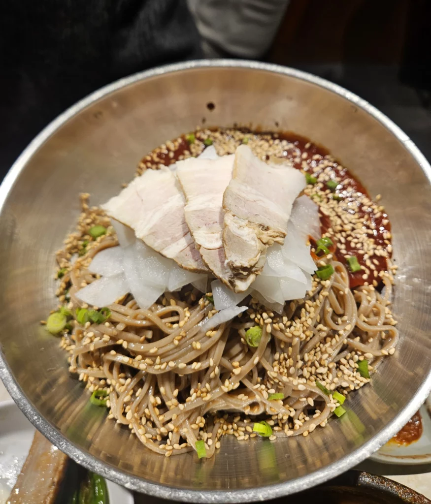 Cold buckwheat noodles garnished with sliced pork, radish, sesame seeds, and spicy sauce, paired with samgyeopsal K-BBQ  at Keum Eun Don.