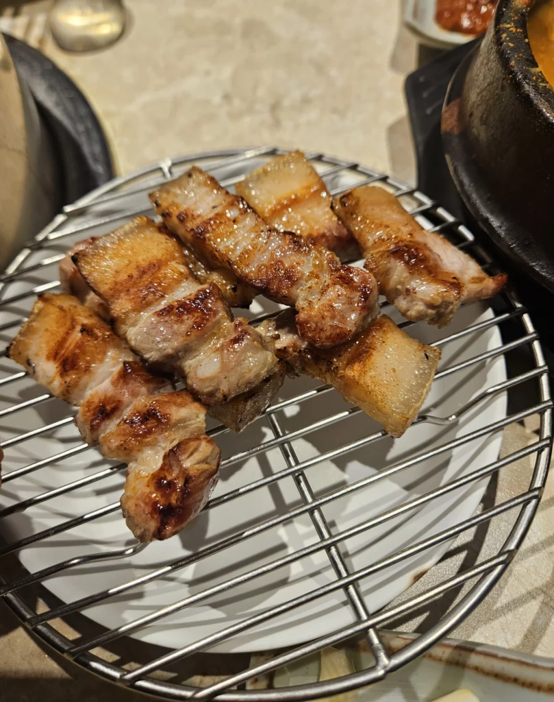 Perfectly grilled samgyeopsal pork belly resting on a metal rack after charcoal cooking at Keum Eun Don K-BBQ restaurant.