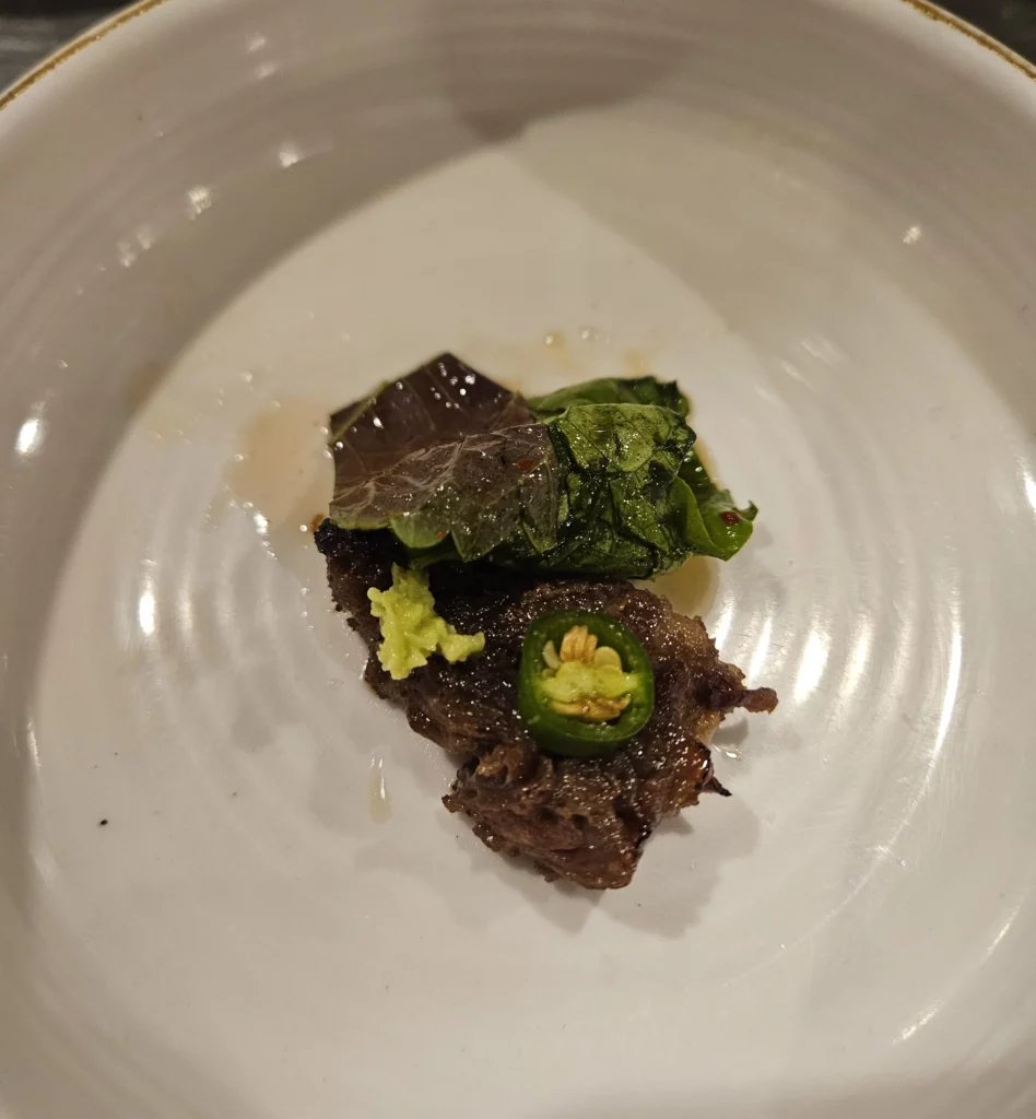 Grilled beef korean bbq served with fresh leafy greens, green chili, and wasabi on a white plate.