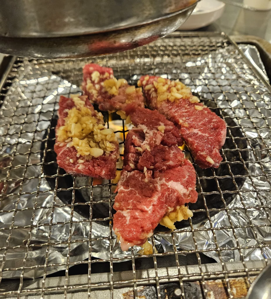 Fresh cuts of beef korean bbq grilling over hot charcoal on a traditional Korean BBQ grill.