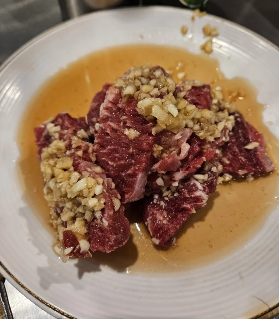Marinated raw beef prepared for beef korean bbq, topped with garlic and sauce on a white plate.