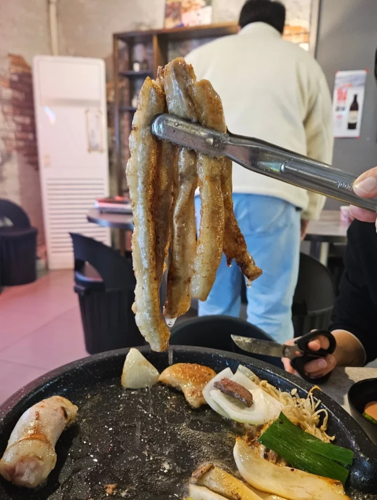 Long strips of freshly grilled gopchang lifted from a sizzling pan, with onions and vegetables cooking together on a Korean BBQ grill.
