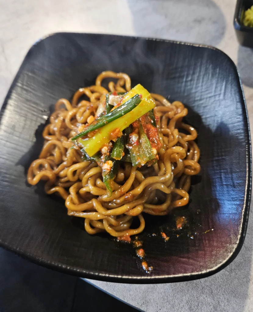 Korean-style noodles topped with scallion kimchi served as a side dish to gopchang, highlighting rich flavors and traditional pairing.