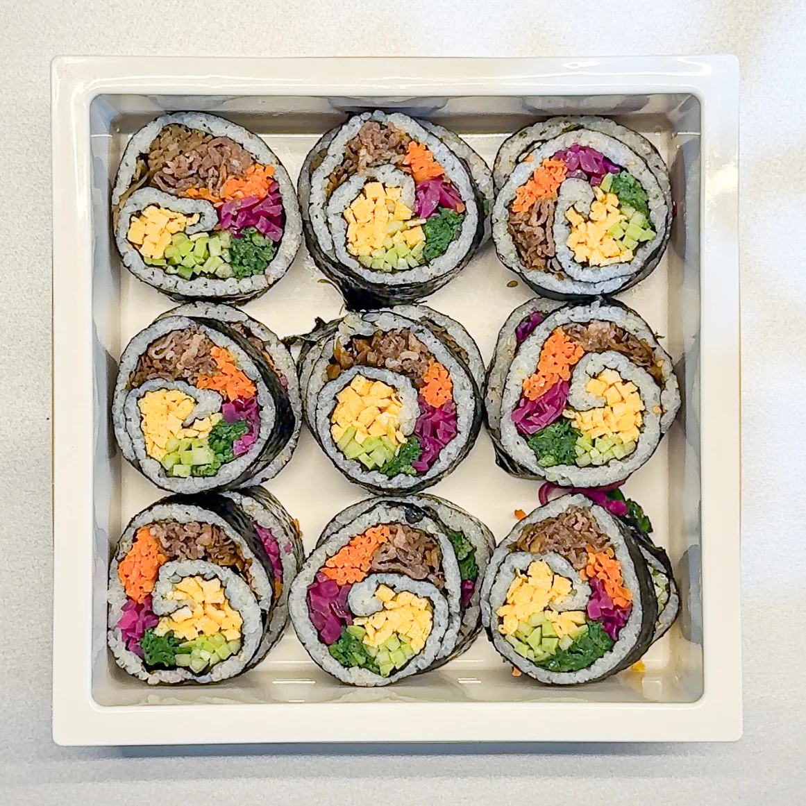 Colorful spiral gimbap slices arranged in a box showing beautiful swirl pattern with bulgogi, vegetables, and egg fillings.