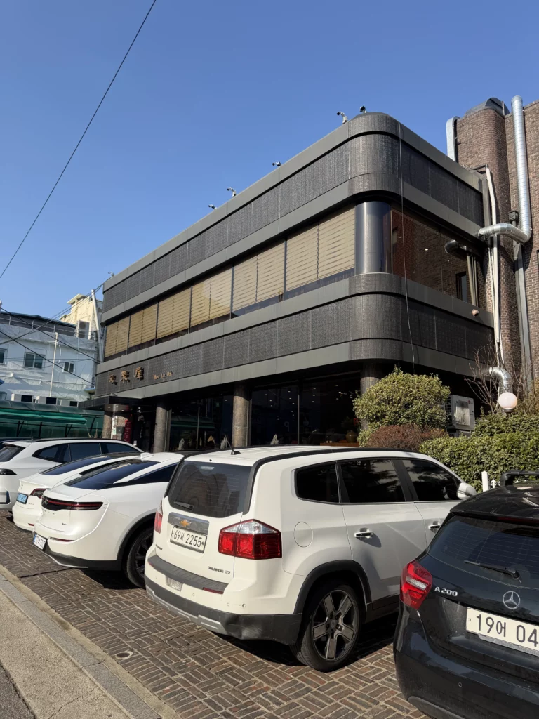 Exterior of Woo Lae Oak restaurant building in Seoul with parking area and cars, showing the modern facade of this historic 78-year-old establishment famous for authentic Pyongyang naengmyeon and premium Hanwoo bulgogi near Euljiro 4-ga Station.