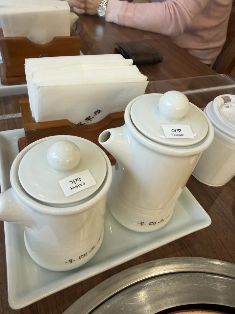 Korean mustard and vinegar condiment containers served tableside at Woo Lae Oak Seoul for customizing traditional Pyongyang naengmyeon, with gyeoja mustard and vinegar used to enhance the flavor of the cold noodle broth.
