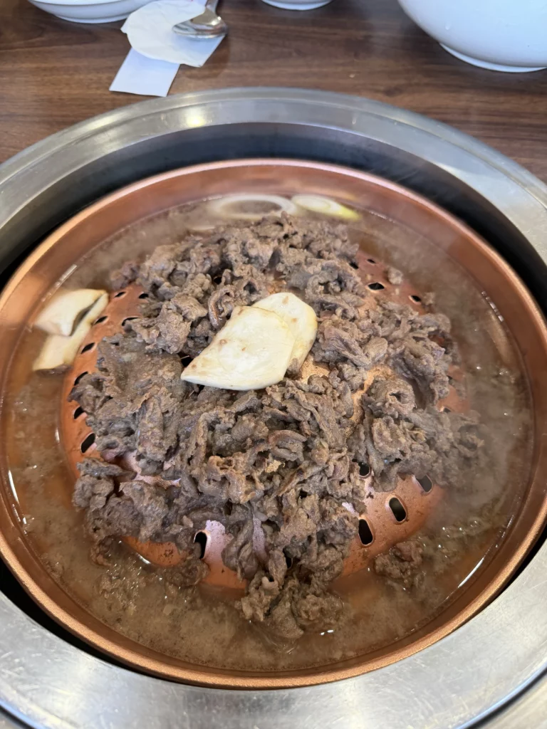 Premium Hanwoo beef bulgogi grilling tableside on a traditional copper plate at Woo Lae Oak Seoul, showing thinly sliced marinated Korean beef with garlic cloves cooking to perfection for the restaurant's signature bulgogi dish.