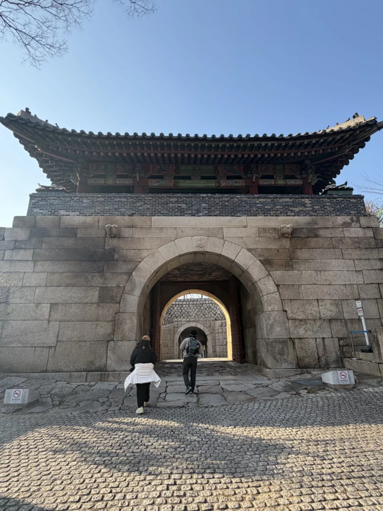 Seoul City Wall traditional Korean fortress gate near Gyeyeolsa restaurant in Buam-dong with hikers approaching Bugaksan Mountain trail.
