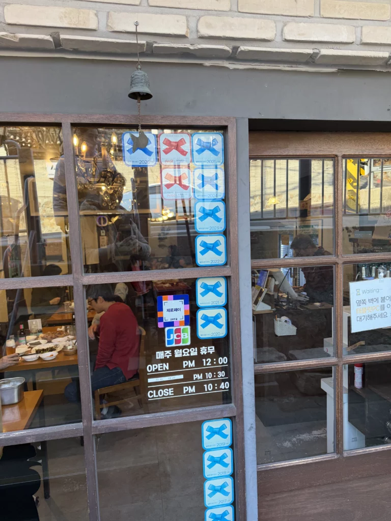 Gyeyeolsa restaurant window with blue chicken logo and operating hours showing 12:00 PM opening for Seoul Korean fried chicken dining in Buam-dong.