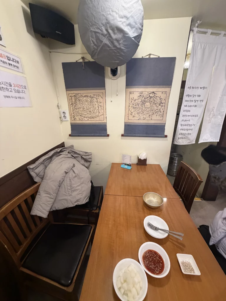 Gyeyeolsa basement restaurant interior with traditional Korean wall art and dining table set with pickled radish and sauces in Buam-dong Seoul.