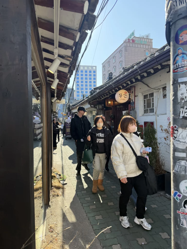 Visitors walking through narrow traditional hanok alleyway in Ikseon-dong Seoul with modern buildings in background.