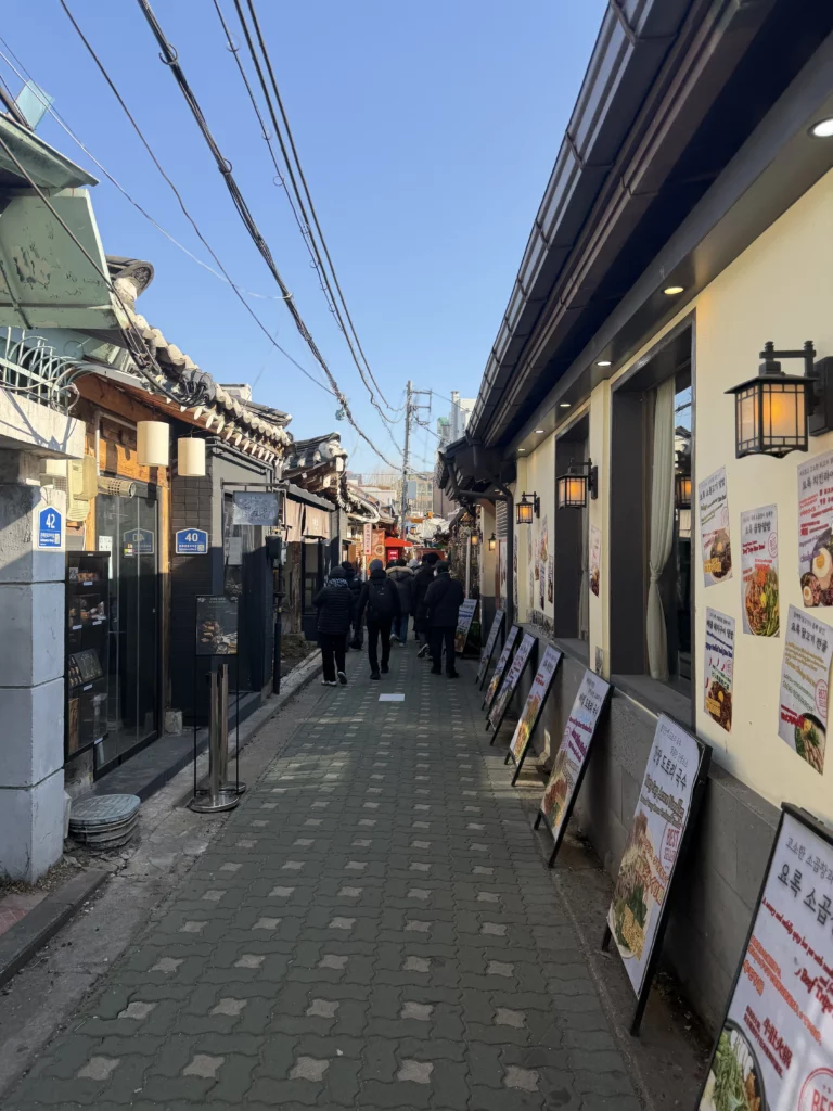 Narrow alleyway in Ikseon-dong hanok village Seoul with traditional Korean architecture, modern cafes, and visitors walking between restaurants near Cheongsu-dang Bakery.