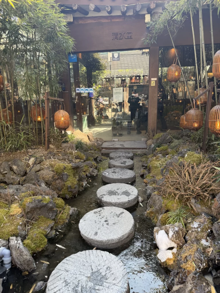 Stepping stones crossing a tranquil pond at Cheongsu-dang Bakery in Ikseon-dong Seoul, framed by bamboo lanterns and moss-covered rocks leading to the traditional hanok cafe entrance.