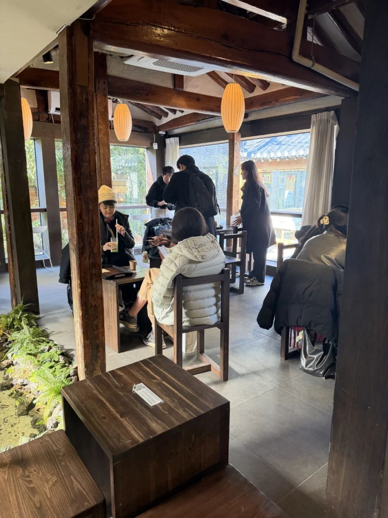 Interior dining room at Cheongsu-dang Bakery with traditional hanok wooden beams, paper lanterns, and customers enjoying souffle castella at this historic Seoul Ikseon-dong cafe.
