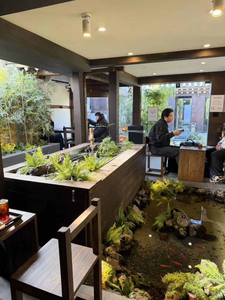 Indoor seating area at Cheongsu-dang Bakery with flowing water feature, koi fish, and moss-covered rocks beneath tables, showcasing the traditional hanok cafe's unique garden design in Seoul Ikseon-dong.