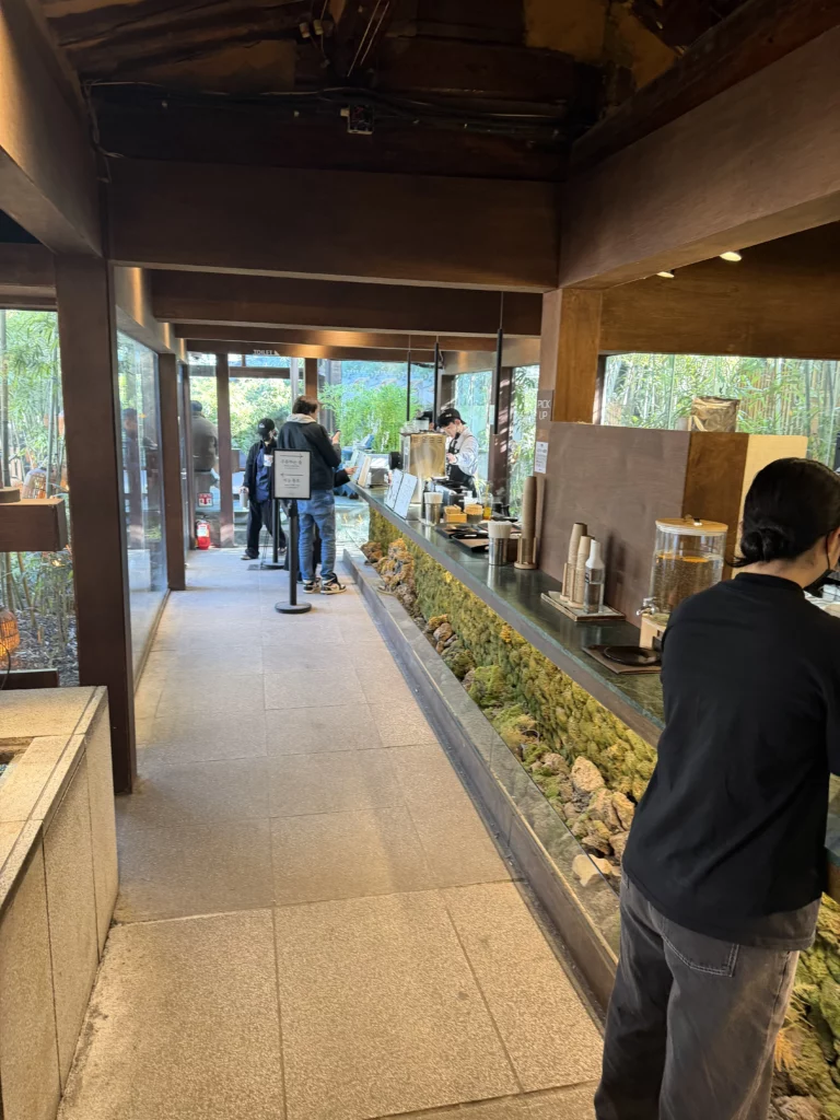 Interior ordering counter at Cheongsu-dang Bakery featuring flowing water features with moss and plants, traditional hanok wooden beams, and bamboo garden views in Seoul's Ikseon-dong cafe.