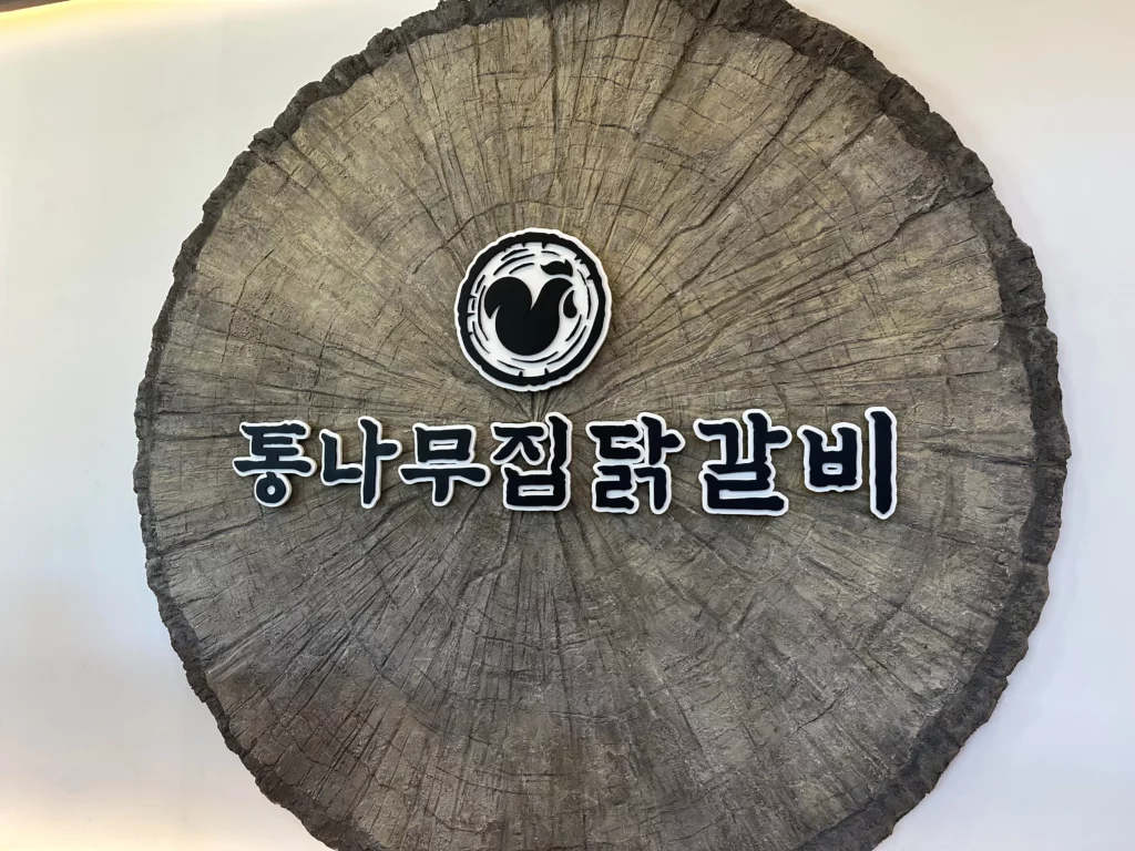 Tongnamujip Dakgalbi logo on wooden log cross-section wall decor representing the charcoal grilled chicken galbi restaurant's wood-fired cooking philosophy.