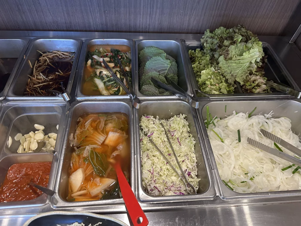 Assorted Korean banchan side dishes including lettuce wraps, napa cabbage, garlic, gochujang sauce, and pickled vegetables served with charcoal grilled chicken galbi at Tongnamujip restaurant in Chuncheon