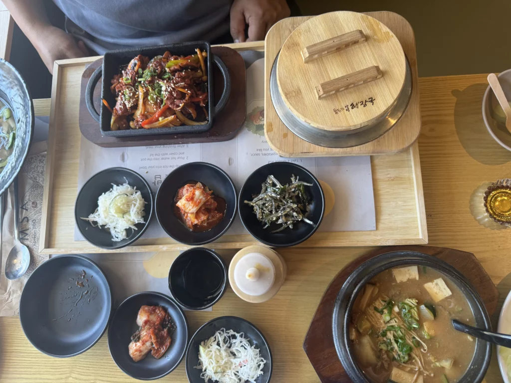 Korean BBQ meal spread with spicy stir-fried dish, hot stone pot rice, banchan, and doenjang jjigae soup.