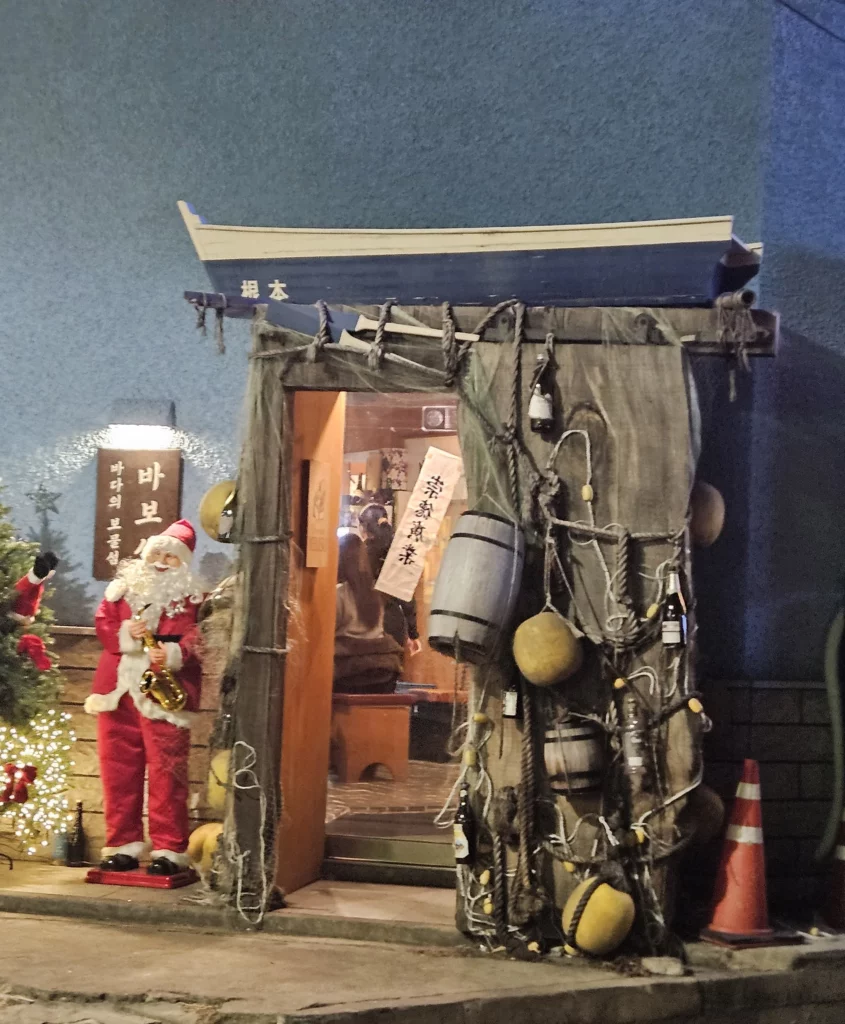 Entrance of a cozy Korean style sashimi and seafood restaurant in Yongsan, decorated with fishing nets and a warm, traditional atmosphere at night.