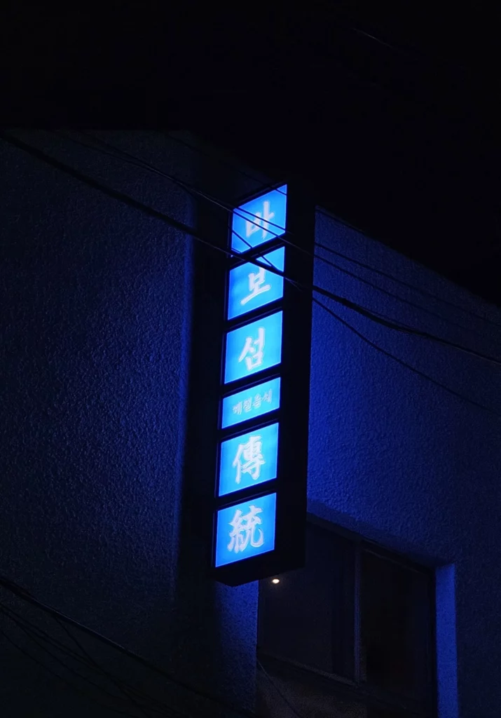 Blue neon sign of a Korean style sashimi and seafood restaurant in Yongsan, glowing at night on the building exterior.
