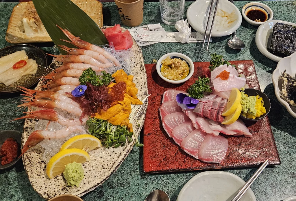 Assorted Korean style sashimi and seafood platter in Yongsan featuring fresh raw fish, shrimp, uni, and garnishes served on ceramic plates.