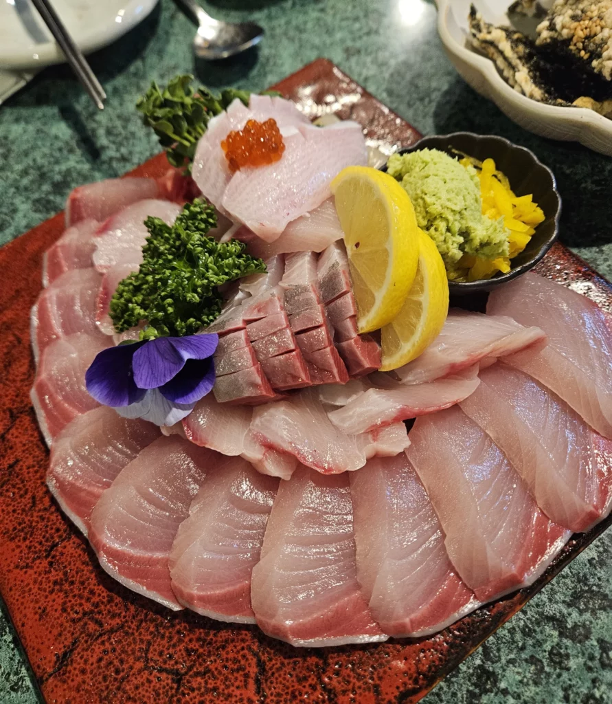 Freshly sliced Korean style sashimi seafood platter in Yongsan, beautifully arranged with raw fish, lemon, wasabi, and garnishes on a ceramic plate.