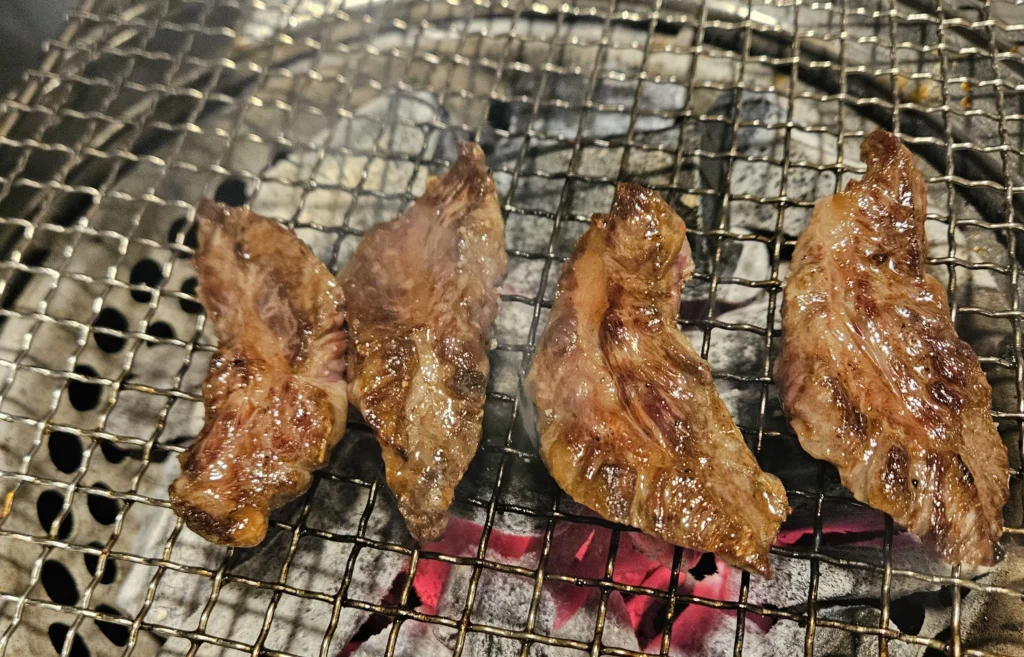 Juicy beef ribs grilling over hot charcoal on a metal grate, showing perfectly seared grilled beef Korean BBQ with smoky char marks.