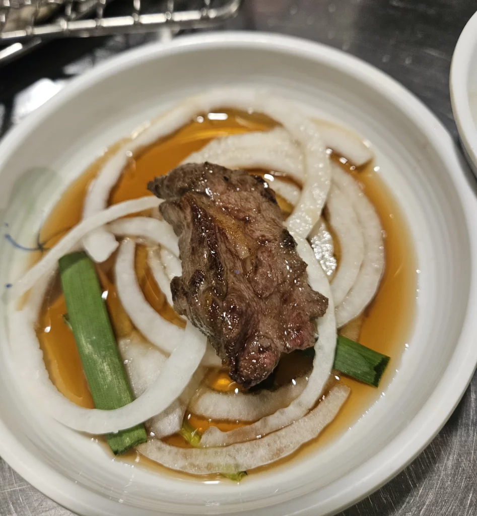 Grilled beef dipped in soy-based sauce with sliced onions and green onions, a classic way to enjoy grilled beef Korean BBQ.