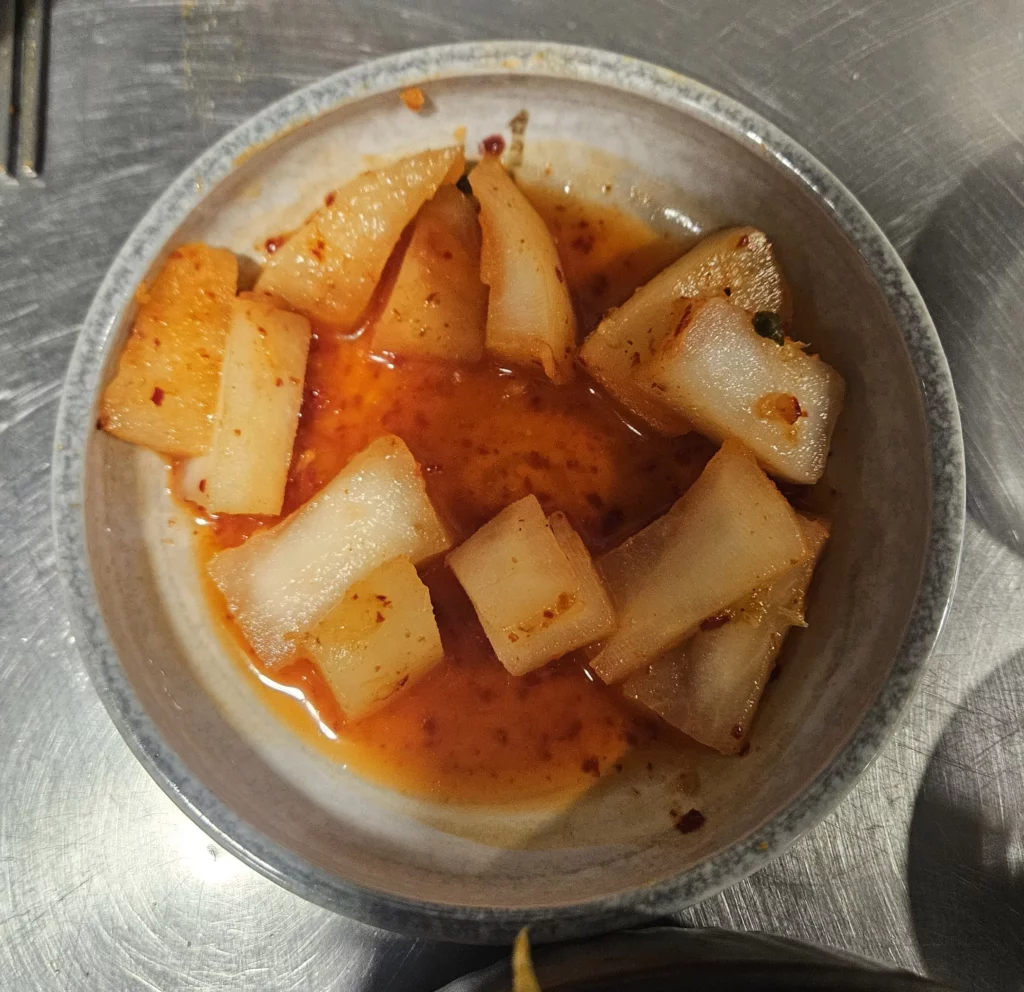 Cubed radish kimchi in spicy chili brine served as a refreshing side dish alongside grilled beef Korean BBQ.