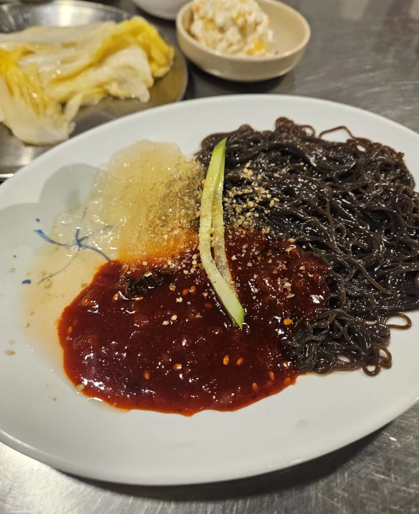 Korean cold buckwheat noodles served with spicy sauce, grated radish, and cucumber, commonly enjoyed as a refreshing side dish after grilled beef Korean BBQ.